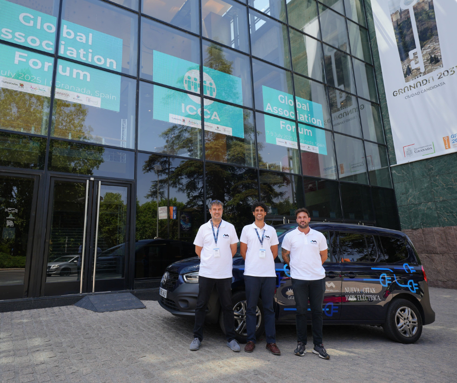 Group of professional corporate drivers in formal uniforms posing outside a modern commercial glass building venue next to an executive fleet vehicle.