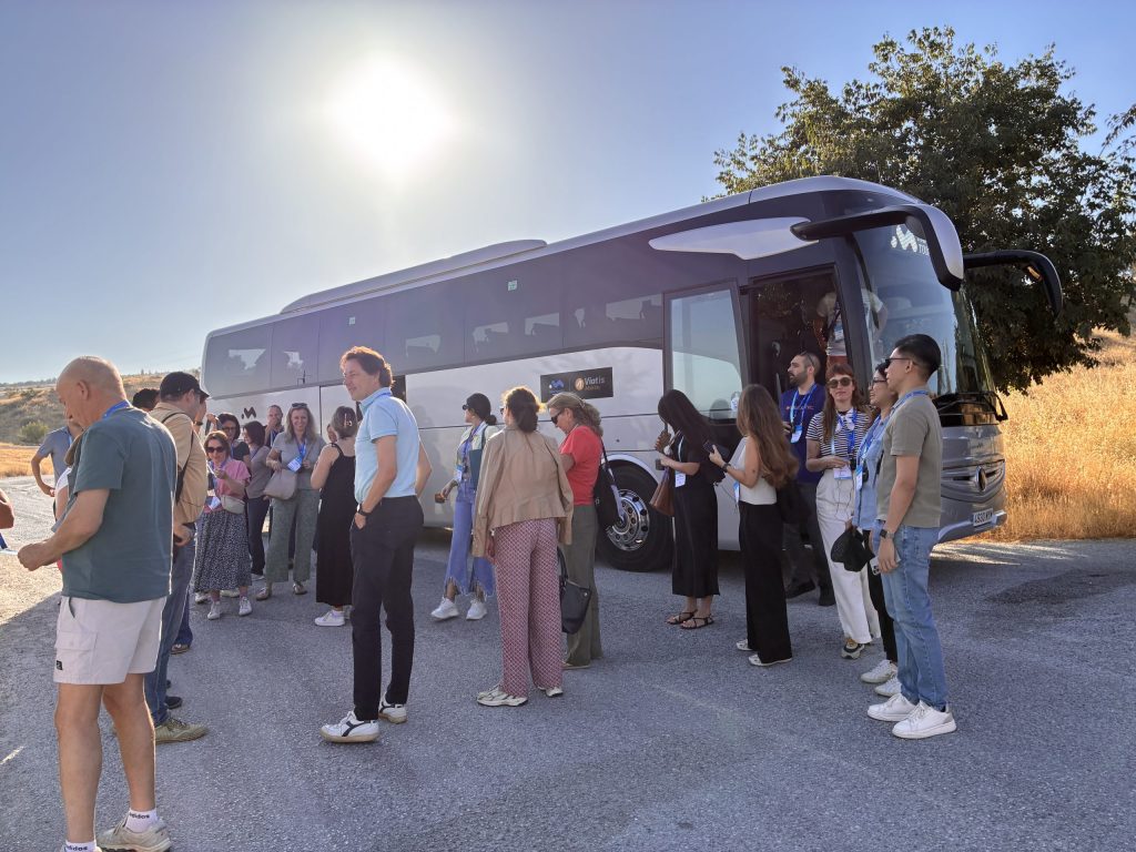 A group of international leisure travelers and corporate delegates gathering outdoors next to a premium private tour bus before starting an excursion.