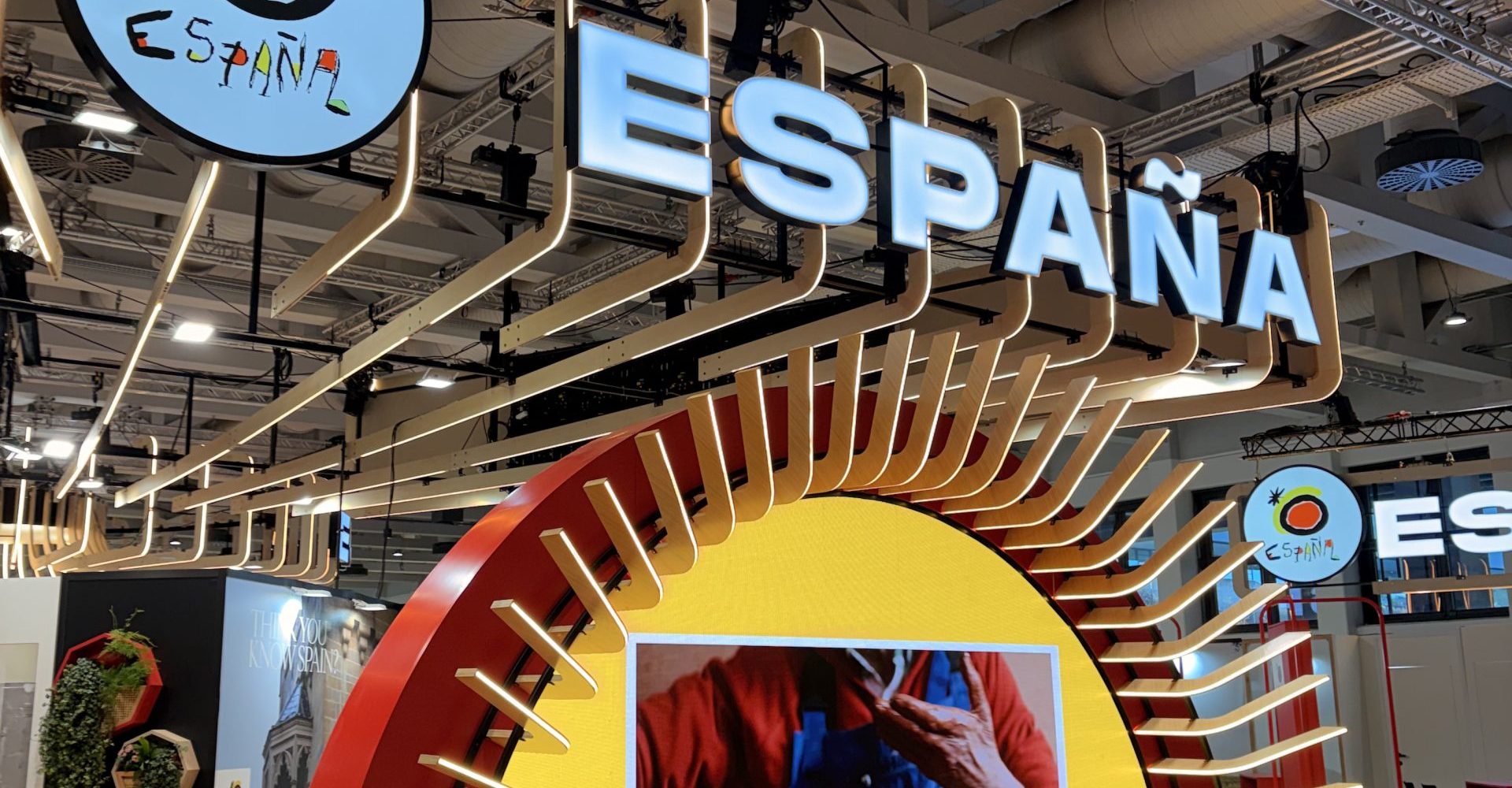 The brightly illuminated official Spain tourism pavilion and corporate exhibition stand at an international travel trade show like ITB Berlin or FITUR.