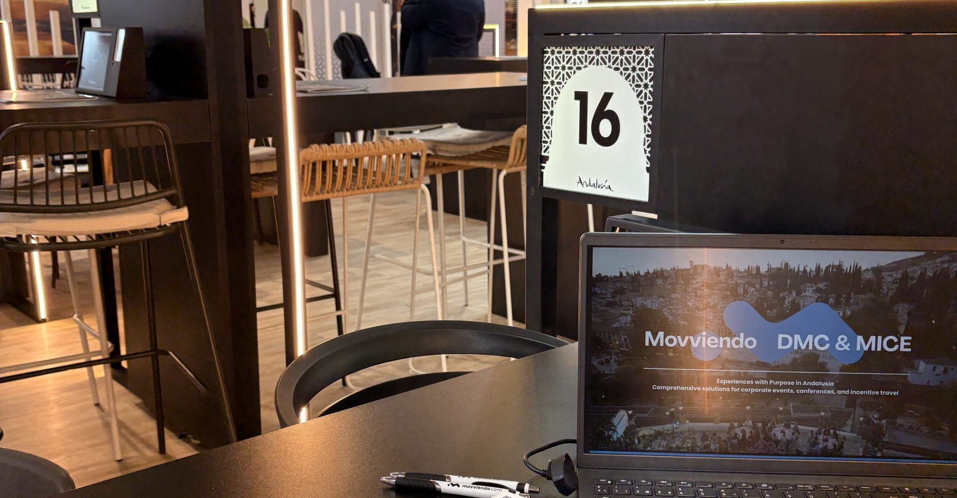 Professional B2B meeting table setup inside the Andalusia pavilion at a tourism trade fair, featuring corporate branding and digital event brochures.