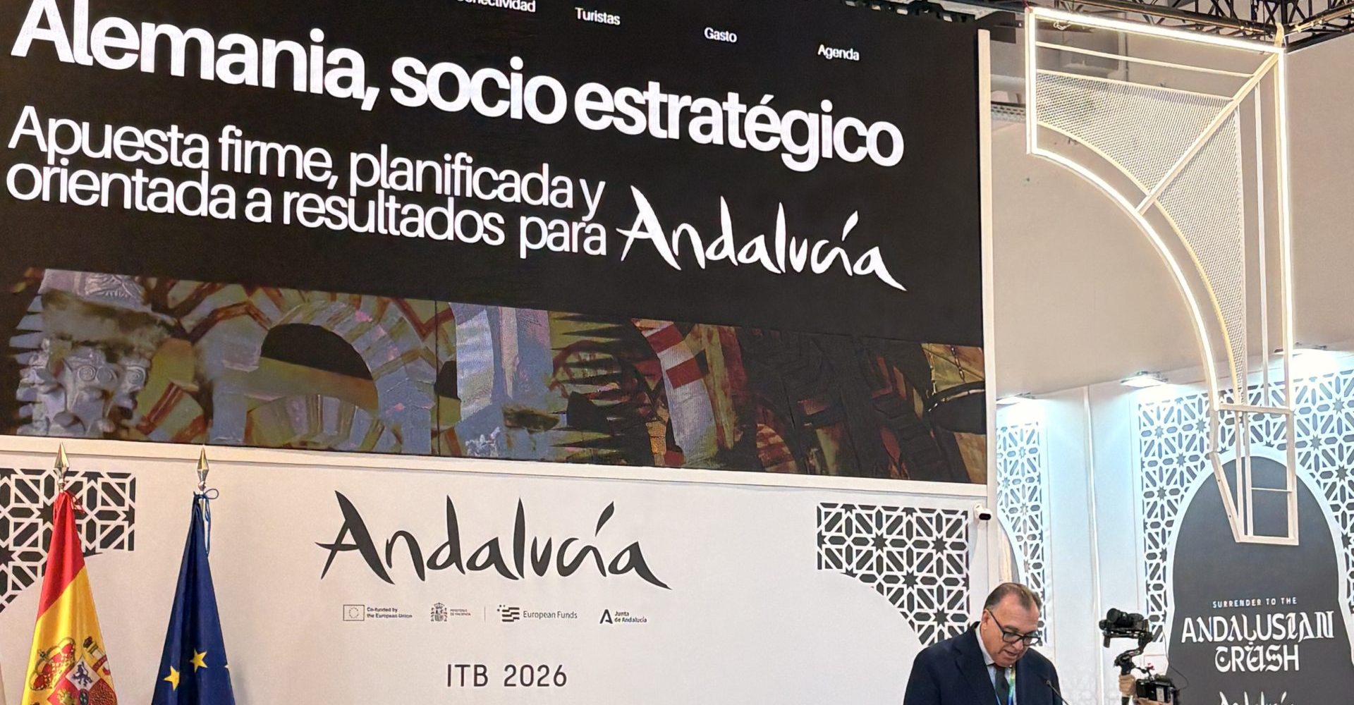 A large promotional screen inside an international tourism fair displaying Germany as a strategic business partner text and official branding from the Andalusia tourism board.