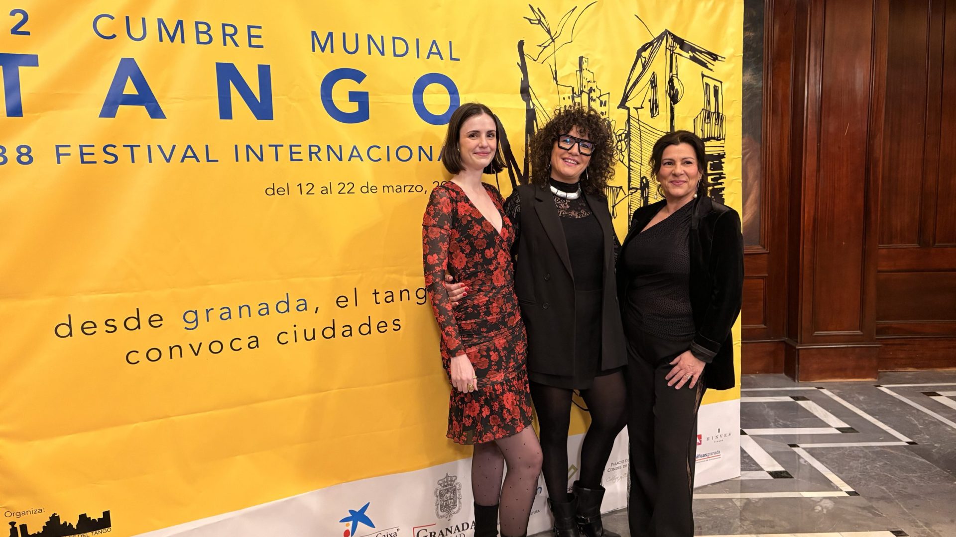 Three corporate representatives posing in front of the yellow Global Tango Summit official banner during a cultural tourism event managed by Movviendo in Granada Andalusia.