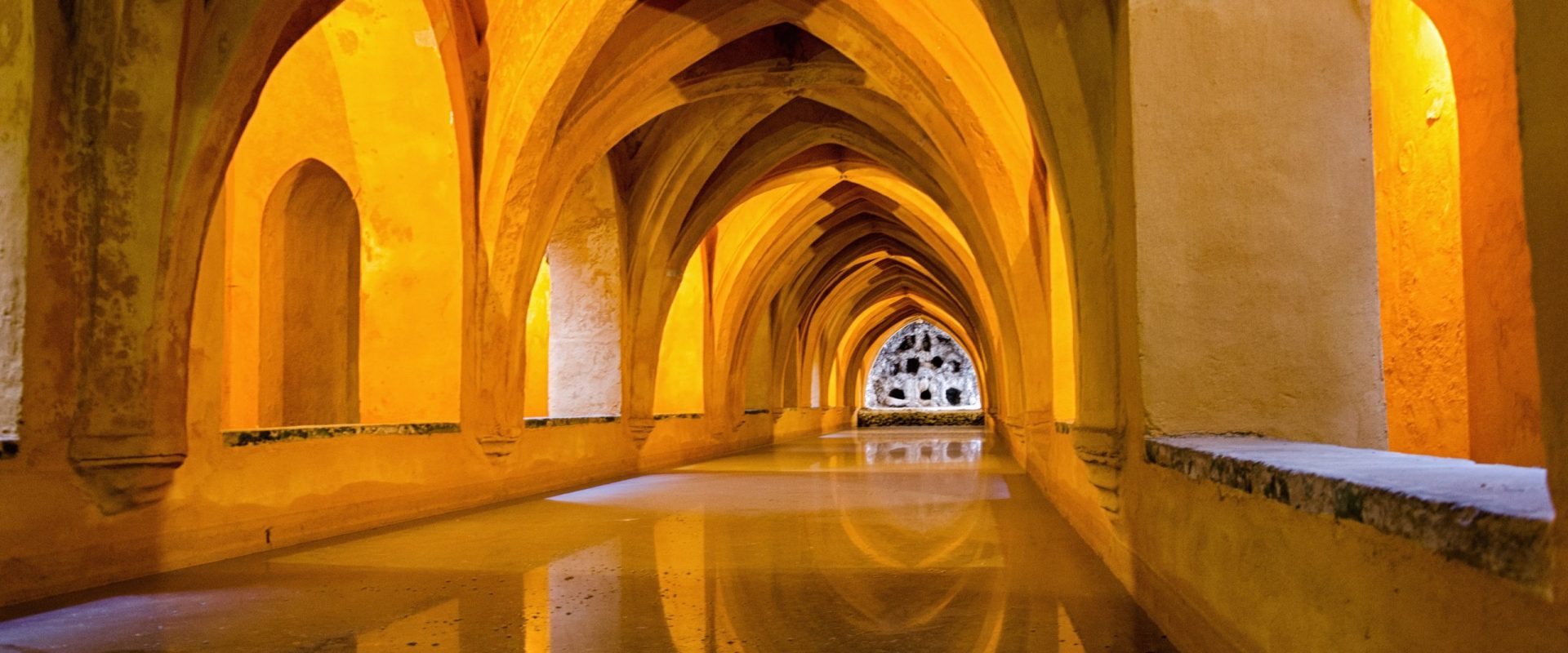 Interior perspective of an ancient historical venue showcasing beautiful golden stone vaults and classic architectural arches illuminated by ambient lighting.