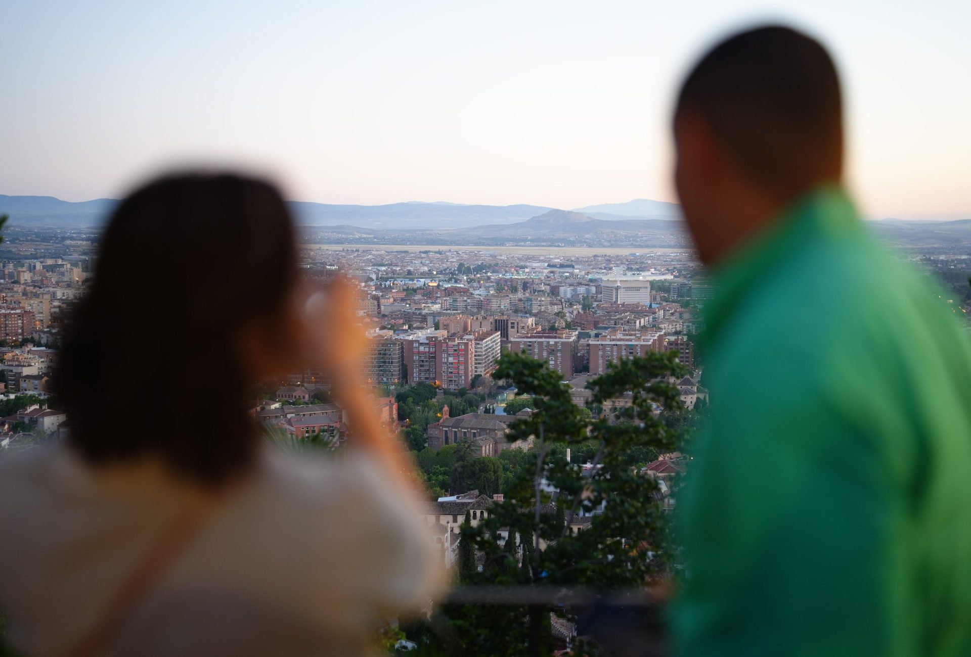 Siluetas desenfocadas de una pareja en primer plano contemplando una panorámica de la ciudad de Granada al atardecer desde un mirador.