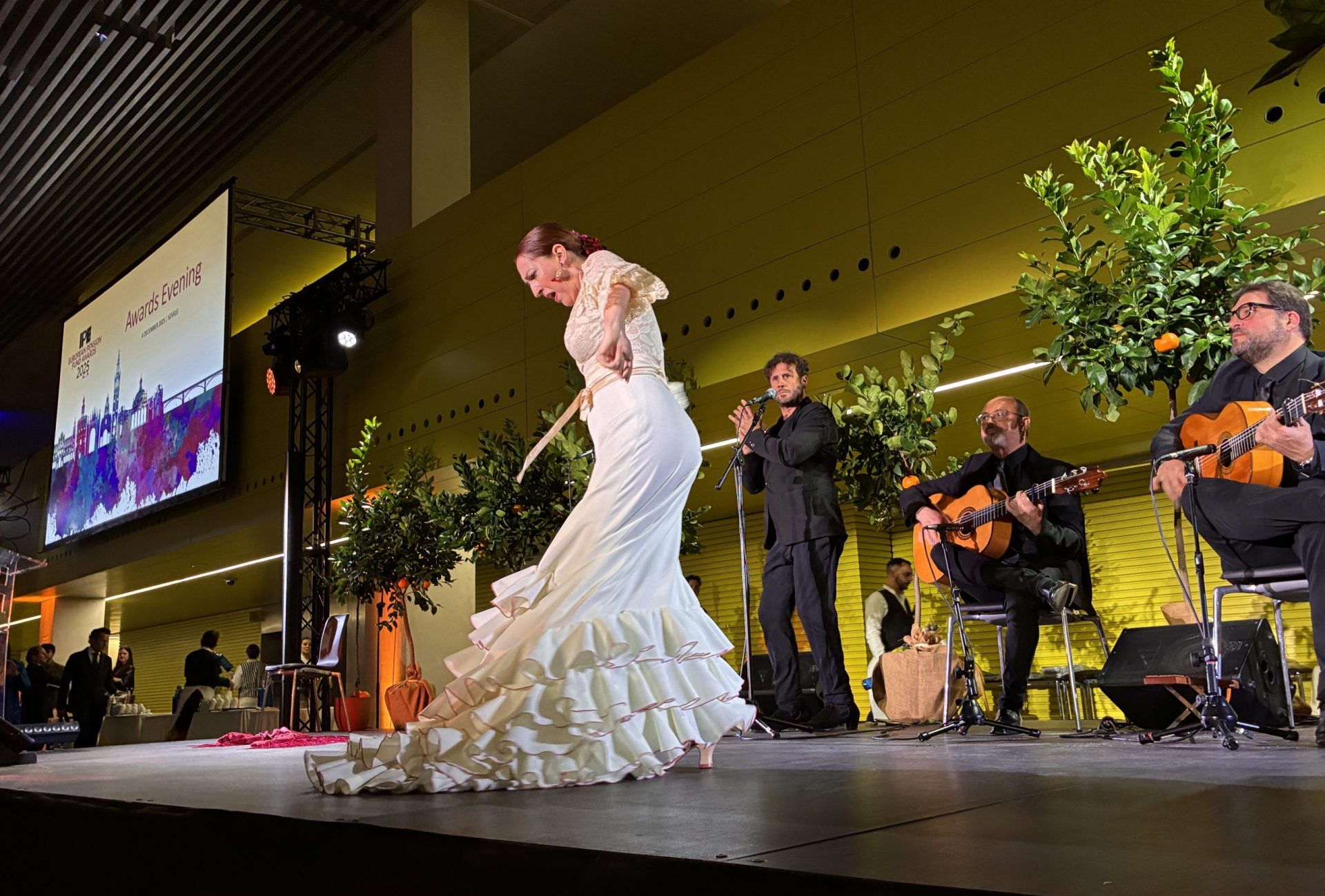 An elegant live musical performance with traditional Spanish artists playing guitars on an illuminated stage during a premium corporate gala dinner.