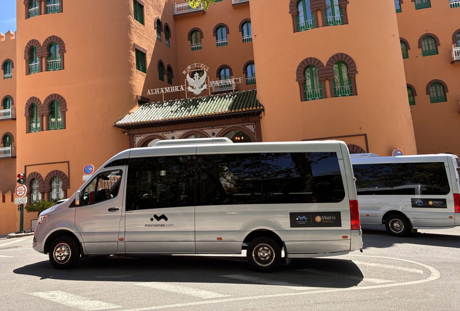 Dos minibuses plateados de la empresa Movviendo aparcados frente a la fachada principal del Hotel Alhambra Palace en Granada durante un servicio de traslado.