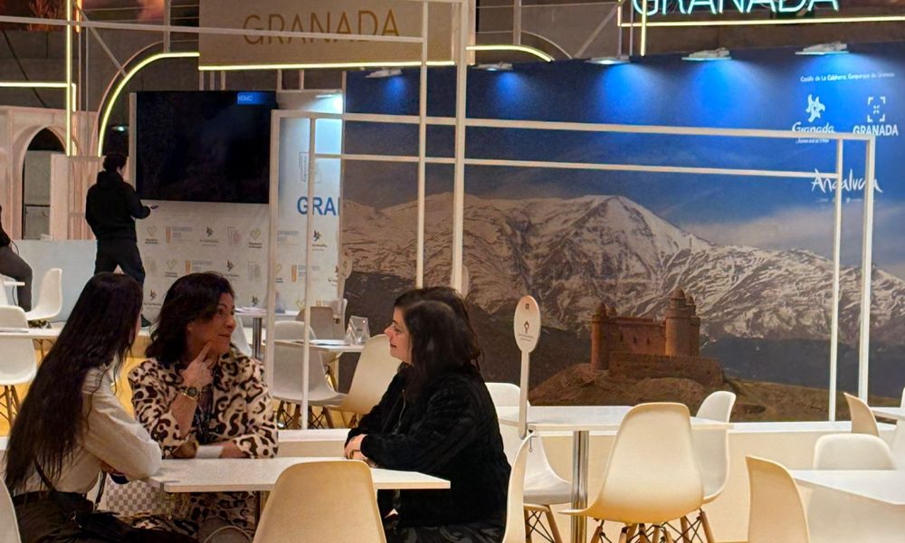 Two professional tourism delegates holding a corporate B2B meeting at the modern Granada exhibition stand inside an international travel trade show.