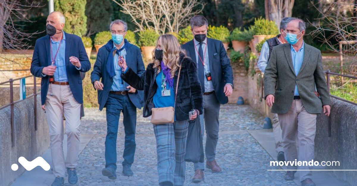 Grupo de personas caminando por un entorno ajardinado mientras escuchan explicaciones de un guía.