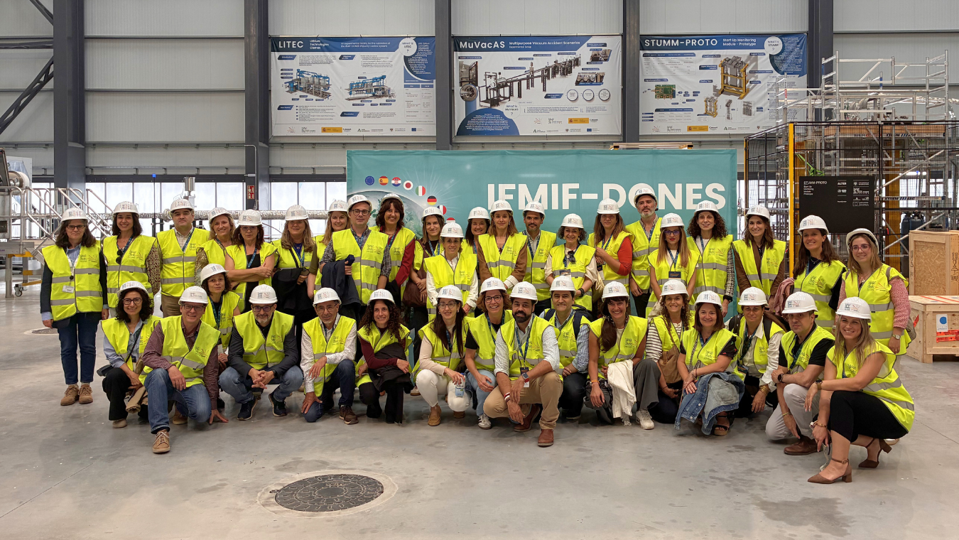 Gran grupo de trabajadores y voluntarios posando juntos con chalecos de seguridad y cascos blancos en un recinto industrial o de eventos.