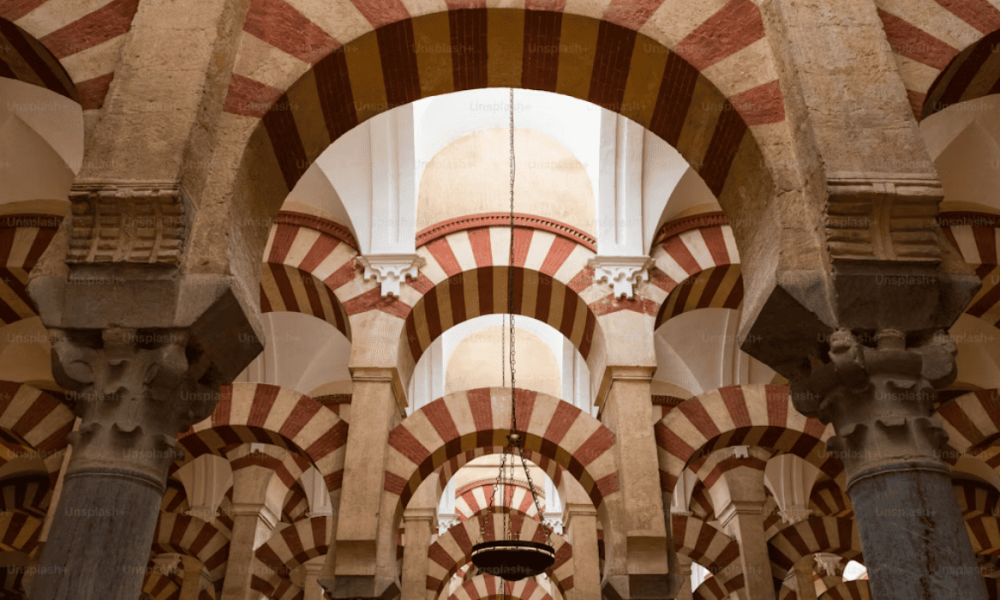 Sucesión de arcos de ladrillo y piedra con franjas bicolores inspirados en la arquitectura califal e islámica.