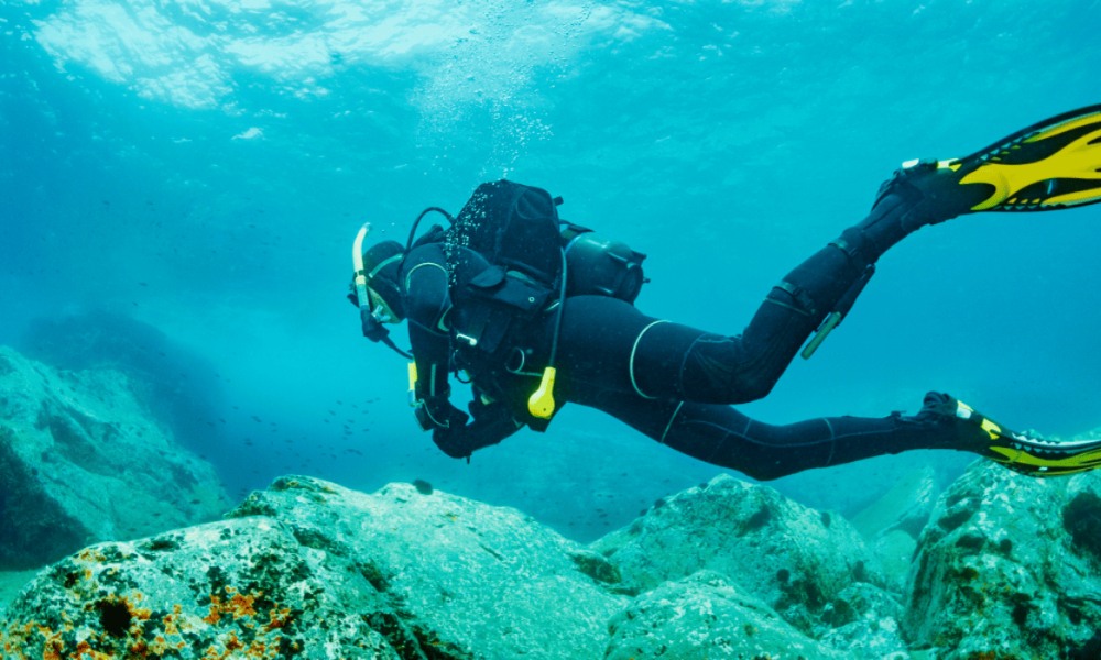 Buceador con traje de neopreno negro y equipo de oxígeno sumergido en aguas marinas azules de la costa de Granada.
