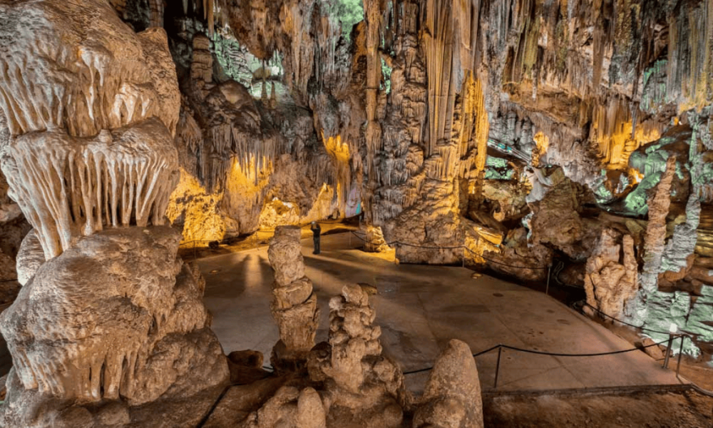 Formaciones de estalactitas y estalagmitas iluminadas artificialmente en el interior de una gran cueva subterránea.