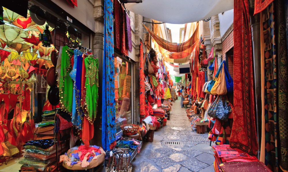 Calle estrecha del mercado de la Alcaicería de Granada con tiendas exteriores que exhiben telas, lámparas árabes y artesanías.