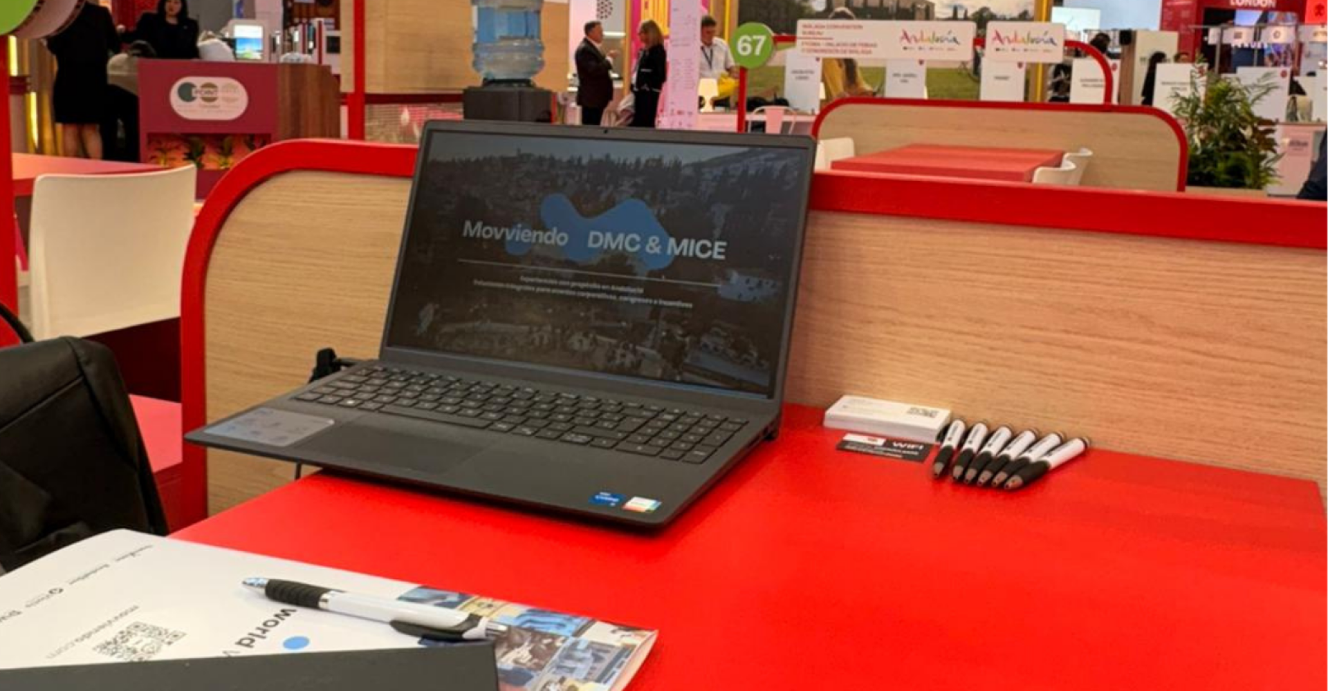 Un ordenador portátil abierto sobre un mostrador rojo corporativo preparado para una presentación digital o registro de clientes en una feria.