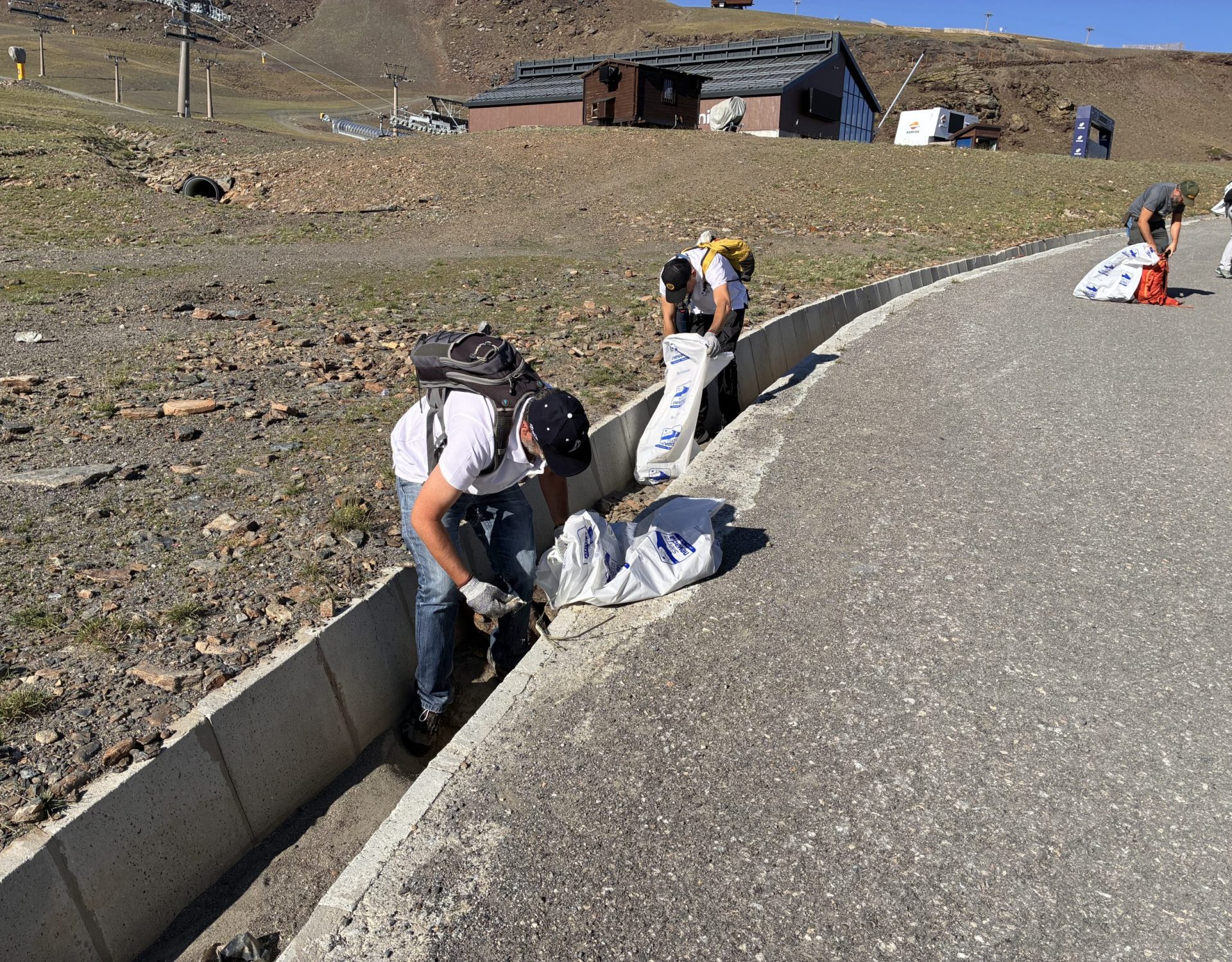 Grupo de voluntarios ambientales caminando y recogiendo residuos por el arcén de una carretera de montaña durante una jornada ecológica.