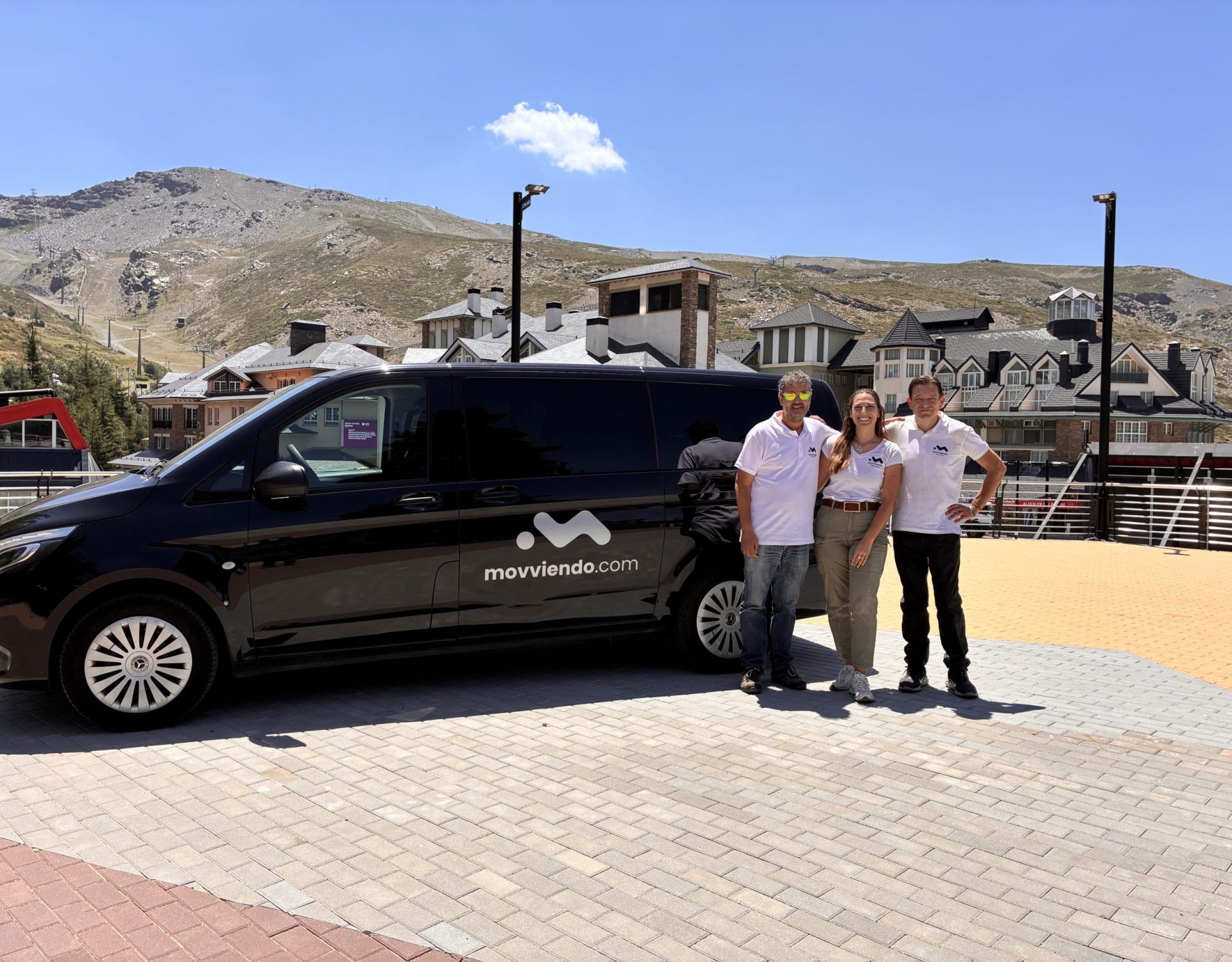 Tres profesionales del equipo de Movviendo posando junto a una furgoneta negra de transporte privado VIP en un entorno de montaña.