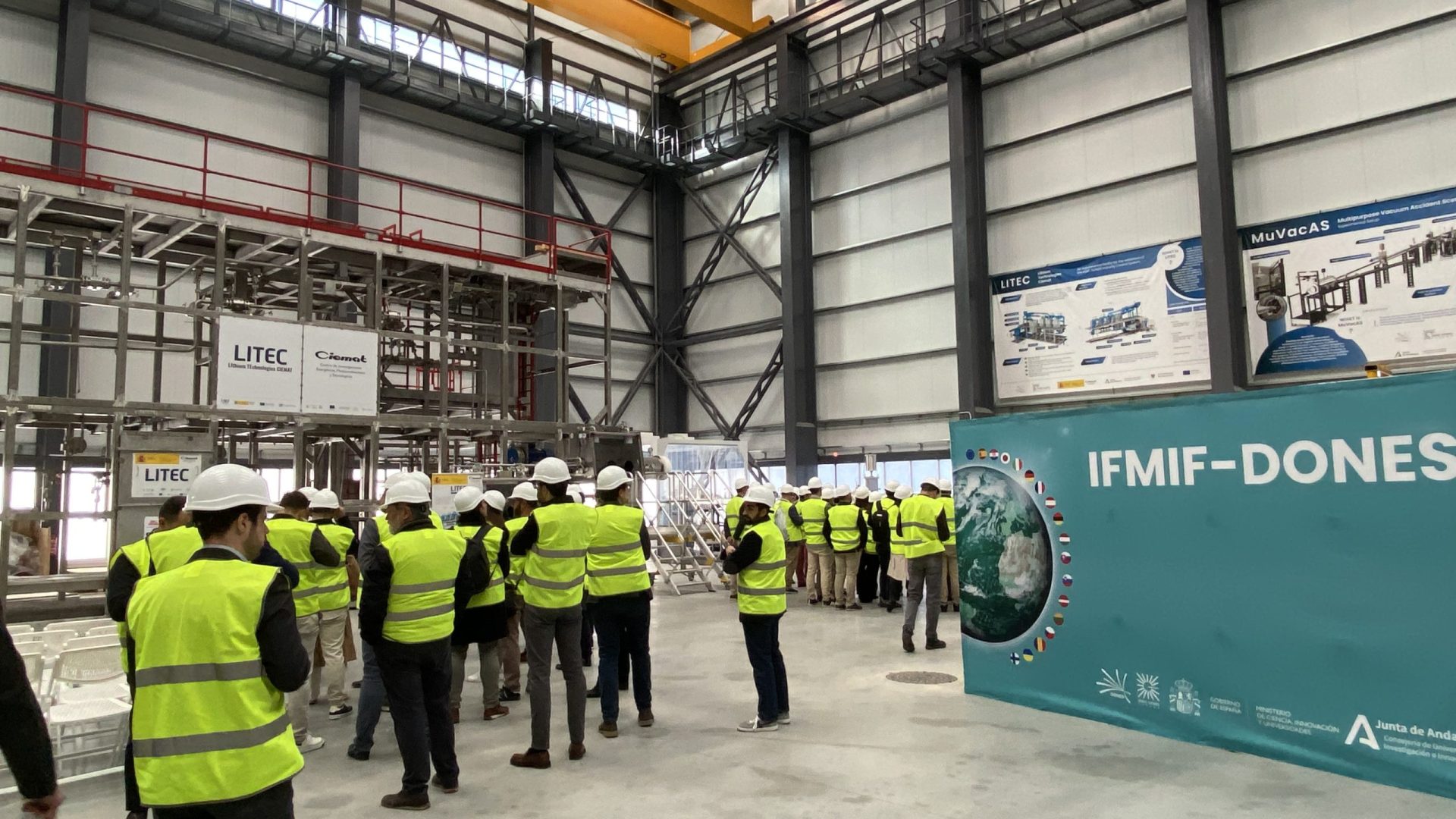 Operarios y técnicos de eventos equipados con chalecos de seguridad coordinando el montaje estructural dentro de un gran pabellón industrial.
