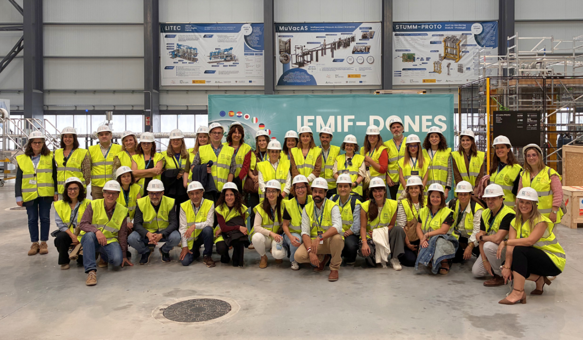 Gran grupo de trabajadores y voluntarios posando juntos con chalecos de seguridad y cascos blancos en un recinto industrial o de eventos.
