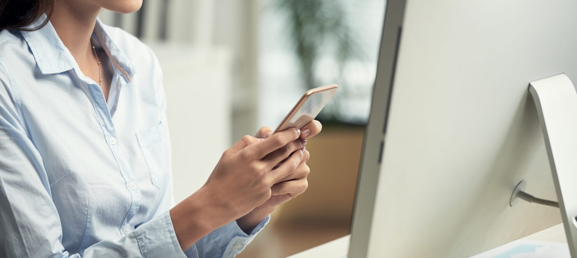 Primer plano de una profesional de oficina utilizando un teléfono móvil inteligente para gestionar reservas en un entorno de trabajo digital.